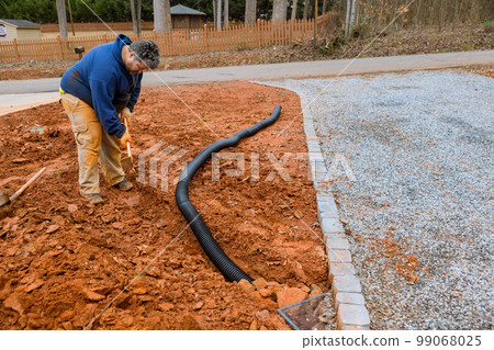 While heavy rainfall is occurring worker digs trench for laying drainage pipe to rainwater 99068025