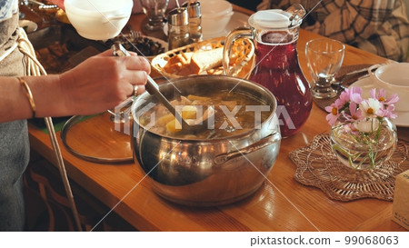 A woman pours hot soup for guests. A woman pours hot soup for guests. 99068063