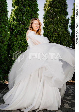 beautiful bride in a white delicate dress dances and spins in the park.  99068118