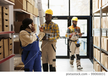 Warehouse manager answering delivery office call and giving instruction to assistant. African american sotrehouse woman operator talking on landline phone and coworker checking order in tablet app Warehouse manager answering delivery office call and giving instruction to assistant. African american sotrehouse woman operator talking on landline phone and coworker checking order in tablet app 99068831