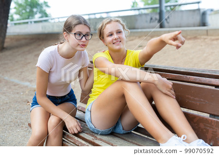 Teenager girls sitting on bench outdoors Teenager girls sitting on bench outdoors 99070592