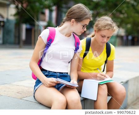 Smart teenager girls doing their homework in city park Smart teenager girls doing their homework in city park 99070622