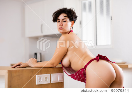 Sensual Latin female in red apron dressed on naked corpus leaning on kitchen table at flat Sensual Latin female in red apron dressed on naked corpus leaning on kitchen table at flat 99070844