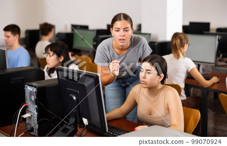 Serious female student explaining the topic to friend while she is studying computer science on the PC in the classroom Serious female student explaining the topic to friend while she is studying computer science on the PC in the classroom 99070924