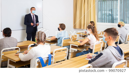 Male teacher in protective mask giving lesson to teenage students Male teacher in protective mask giving lesson to teenage students 99070927