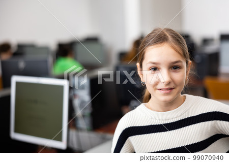 Smiling teen schoolgirl standing in computer class ready for lesson Smiling teen schoolgirl standing in computer class ready for lesson 99070940