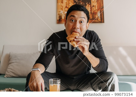 Man having bread and juice as breakfast on the sofa living room. Man having bread and juice as breakfast on the sofa living room. 99073154