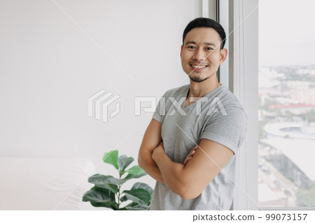 Ordinary happy life smile face asian man stand by the window in his house. Ordinary happy life smile face asian man stand by the window in his house. 99073157