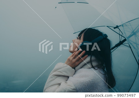 Photo of a woman listening to music with an umbrella in the background of the city 99073497