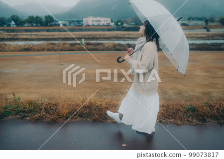一張女性在河床上打傘並使用智能手機的照片 99073817