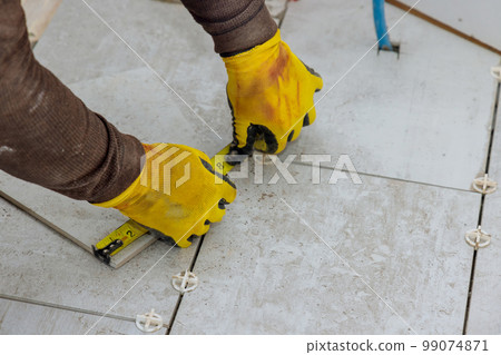 As contractor prepares to lay ceramic tiles on floor he measures tiles prior for cutting them 99074871