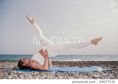 Woman sea yoga. Well looking middle aged woman with braids dreadlocks in white leggings and tops doing stretching pilates on yoga mat near sea. Female fitness yoga routine concept. Healthy lifestyle. Woman sea yoga. Well looking middle aged woman with braids dreadlocks in white leggings and tops doing stretching pilates on yoga mat near sea. Female fitness yoga routine concept. Healthy lifestyle. 99077516