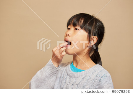 Elementary school girl taking medicine indoors 99079298