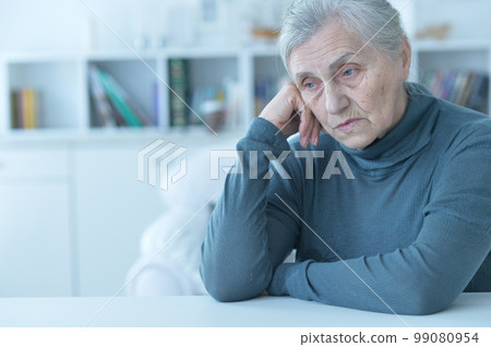 sad senior woman sitting at table 99080954