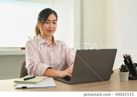 Confident female office worker watching online presentation on laptop computer at modern workplace Confident female office worker watching online presentation on laptop computer at modern workplace 99081535