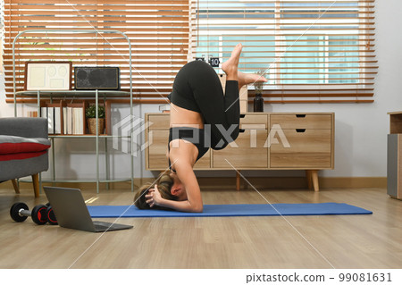 Young sporty woman doing yoga exercise, doing handstand pose on mat. Health care and exercise at home concept Young sporty woman doing yoga exercise, doing handstand pose on mat. Health care and exercise at home concept 99081631