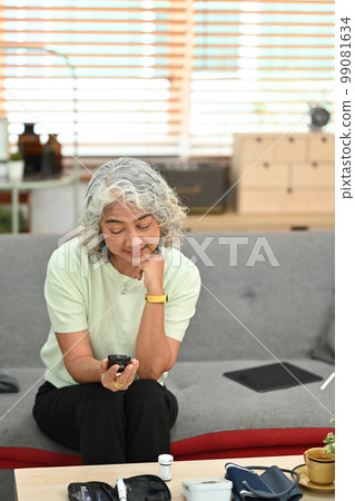 Senior woman sitting on couch and checking blood glucose levels with a glucose meter. Diabetes and health care concept 99081634
