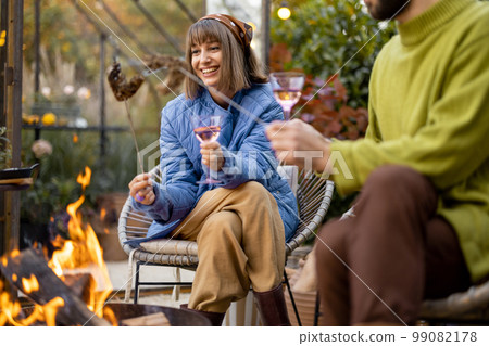 Young couple spending dinner time by the fire at backyard 99082178