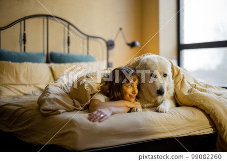 Woman with her dog under the blanket on bed Woman with her dog under the blanket on bed 99082260