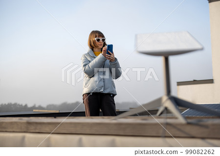 Woman uses satellite internet connection on roof of a house Woman uses satellite internet connection on roof of a house 99082262