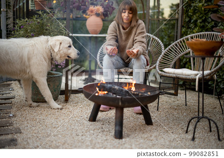 Woman with a dog by the fire at backyard 99082851