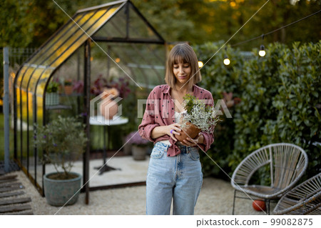 Woman with flowerpot in garden with greenhouse behind Woman with flowerpot in garden with greenhouse behind 99082875