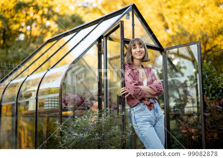 Woman near greenhouse with flowers at back yard Woman near greenhouse with flowers at back yard 99082878