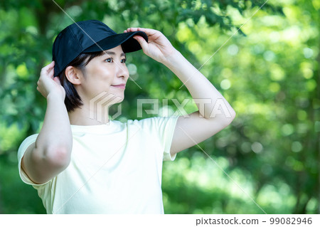 A woman wearing a hat refreshing in the fresh green 99082946