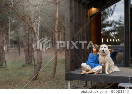Woman rests with a dog near wooden cottage in nature 99083343