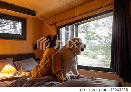 Woman with a dog lying on bed at wooden cabin on nature Woman with a dog lying on bed at wooden cabin on nature 99083358