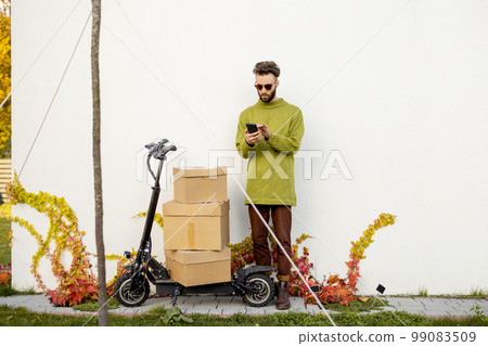 Man with phone near scooter and parcels outdooors Man with phone near scooter and parcels outdooors 99083509