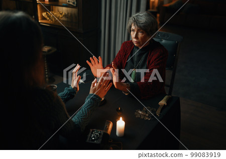 Fortune teller sorceress and woman doing spiritual ritual over candle flame 99083919