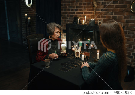 Female enchantress witch spreading tarot cards at table front of client 99083938
