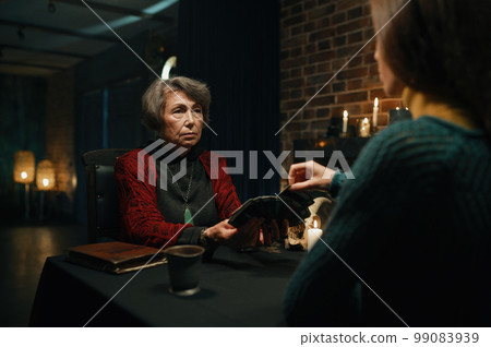 Old mature soothsayer holding divination tarot cards in front of client 99083939
