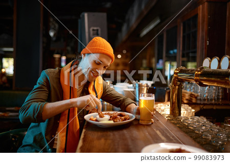 Young man football fan eating snack and drinking beer in sports bar Young man football fan eating snack and drinking beer in sports bar 99083973