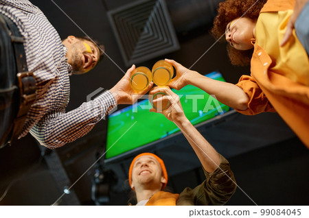Group of friends celebrating win clinking beer glasses in sports bar 99084045