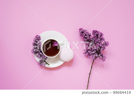Tea cup with marshmallow dessert and lilac flowers on a pink background. Tea cup with marshmallow dessert and lilac flowers on a pink background. 99084419