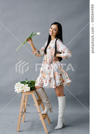 Beautiful girl in a white dress with flowers tulips in her hands on a gray background 99084499
