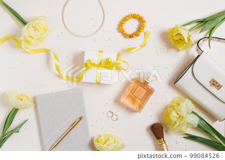 Workplace with a notebook and a pen, yellow tulips, a bracelet, a women's handbag, eau de toilette on a light background. Flat composition for bloggers, magazines, social media and artists. Top view 99084526