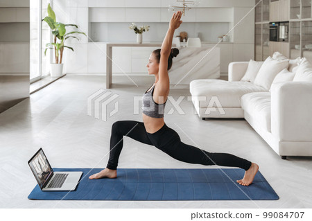 Sporty girl practicing yoga at home using laptop Sporty girl practicing yoga at home using laptop 99084707