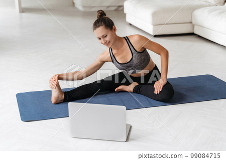 Pretty woman doing stretching opposite laptop in her room Pretty woman doing stretching opposite laptop in her room 99084715