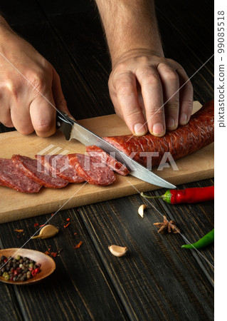 The cook cuts the sausage into small pieces for making sandwiches. Street food idea. 99085518