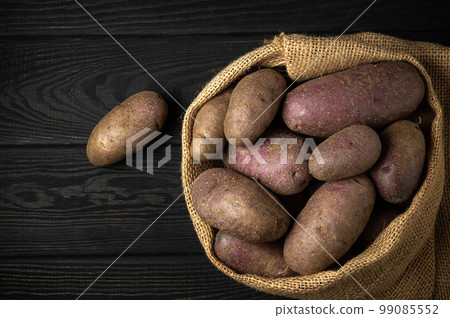 Sack of potatoes after harvest on dark vintage wooden planks. Organic potato for cooking. Free advertising space. 99085552