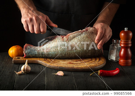 Chef or cook is cleaning bighead carp fish. Working environment in the restaurant kitchen. Fish diet concept 99085566