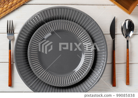Glossy grey ceramic plate with cutlery on wooden table 99085838