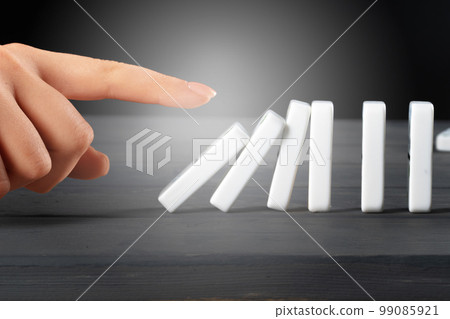 Woman hand toppling dominoes. Chain reaction business concept Woman hand toppling dominoes. Chain reaction business concept 99085921