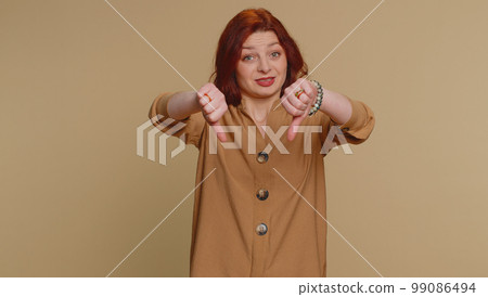 Upset young woman girl in blouse showing thumbs down sign gesture, disapproval, dissatisfied dislike 99086494