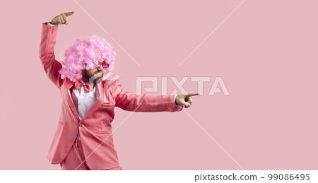 Funny man in clown wig points his fingers away showing something on pink background 99086495