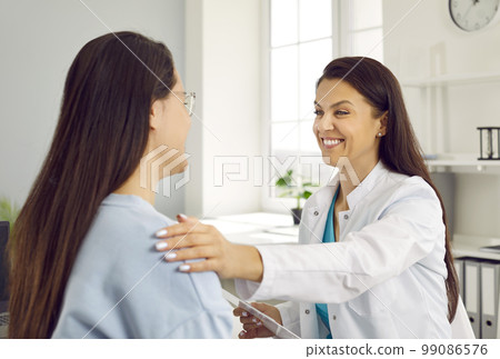 Friendly smiling female doctor holding woman's shoulder telling her positive news about her health. 99086576