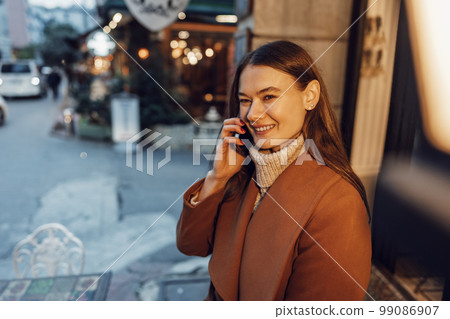 Young happy woman talking on the phone in the street 99086907